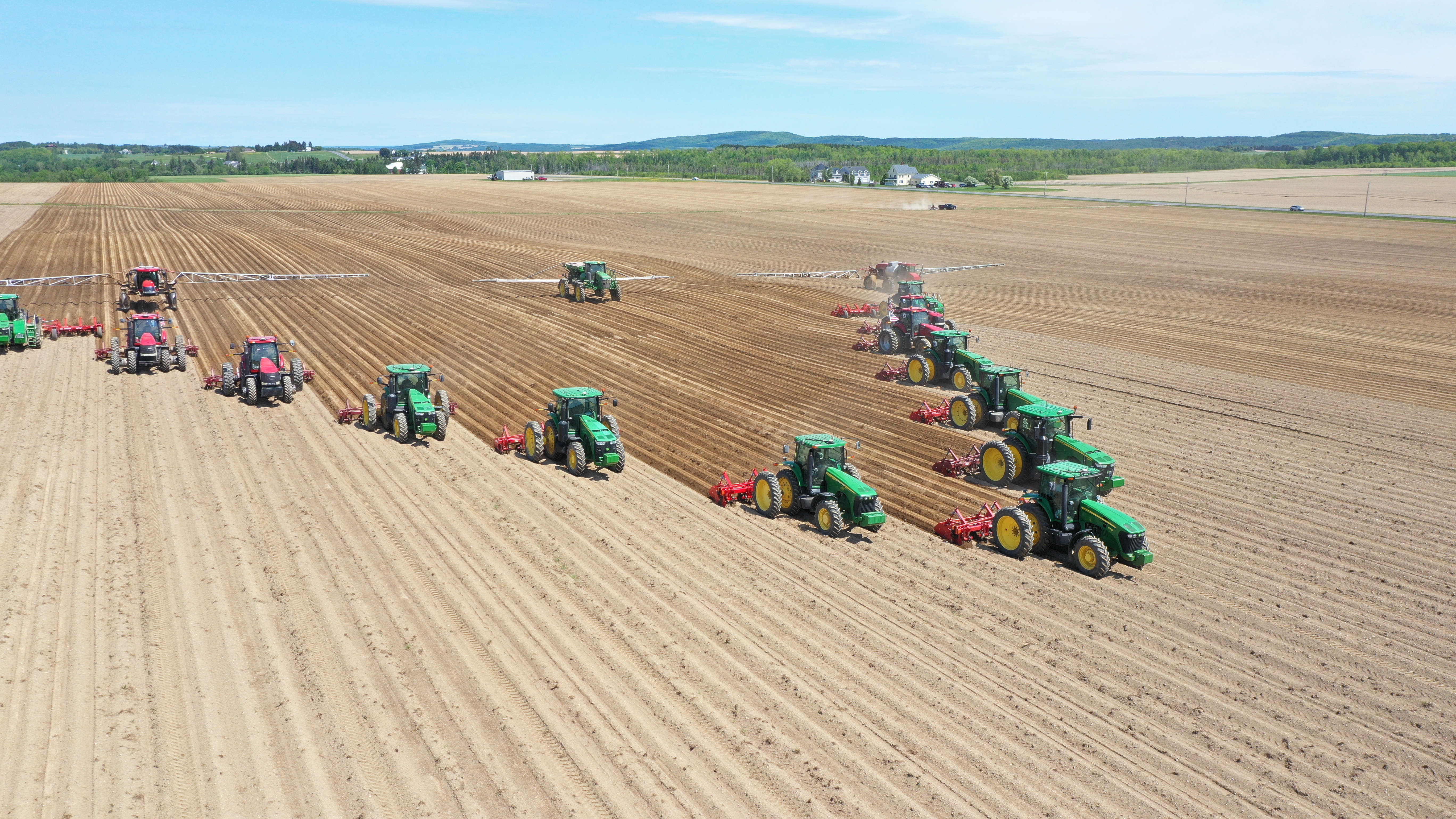 aerial photo of several tractors in v formation planting potatos in newly plowed field